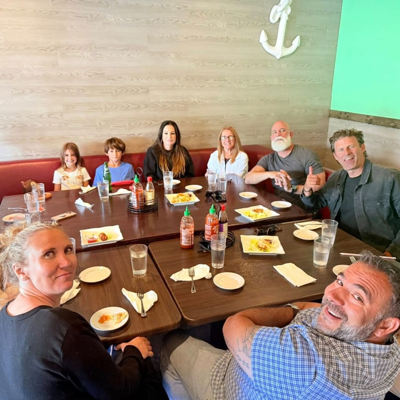 A group of people, including children, smiling and dining at a Mexiyaki restaurant table.