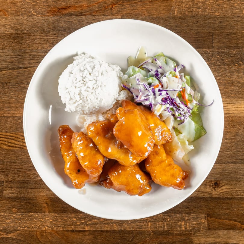A white plate of Mexiyaki's orange chicken, white rice, and coleslaw on a wooden table.