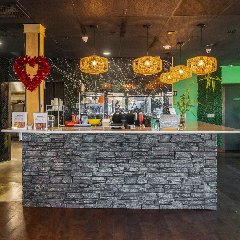 A stone-faced counter with drinks, menus, and Asian-inspired decor under woven pendant lights.
