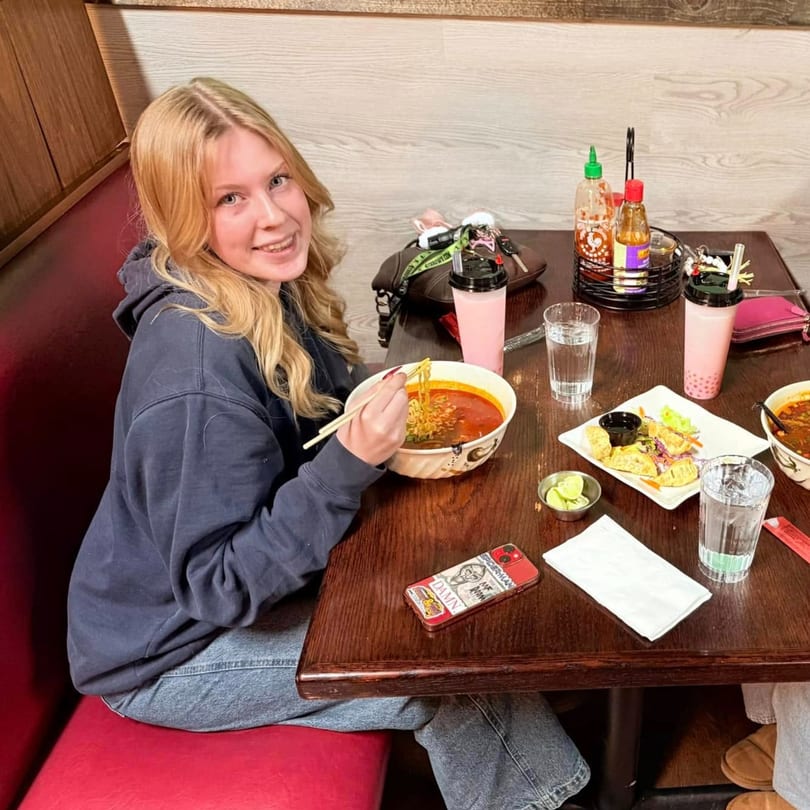 Blonde woman smiling while eating a large bowl of ramen noodles with chopsticks at Mexiyaki.